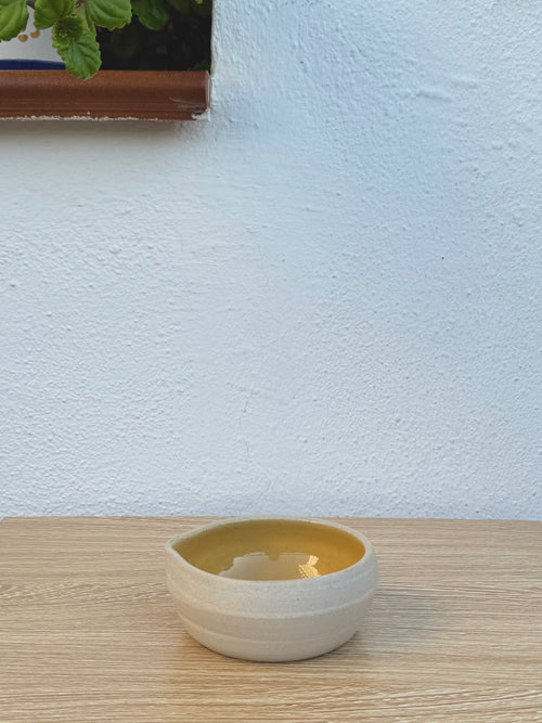 Small ceramic bowl with mustard yellow interior and pouring spout on wooden table
