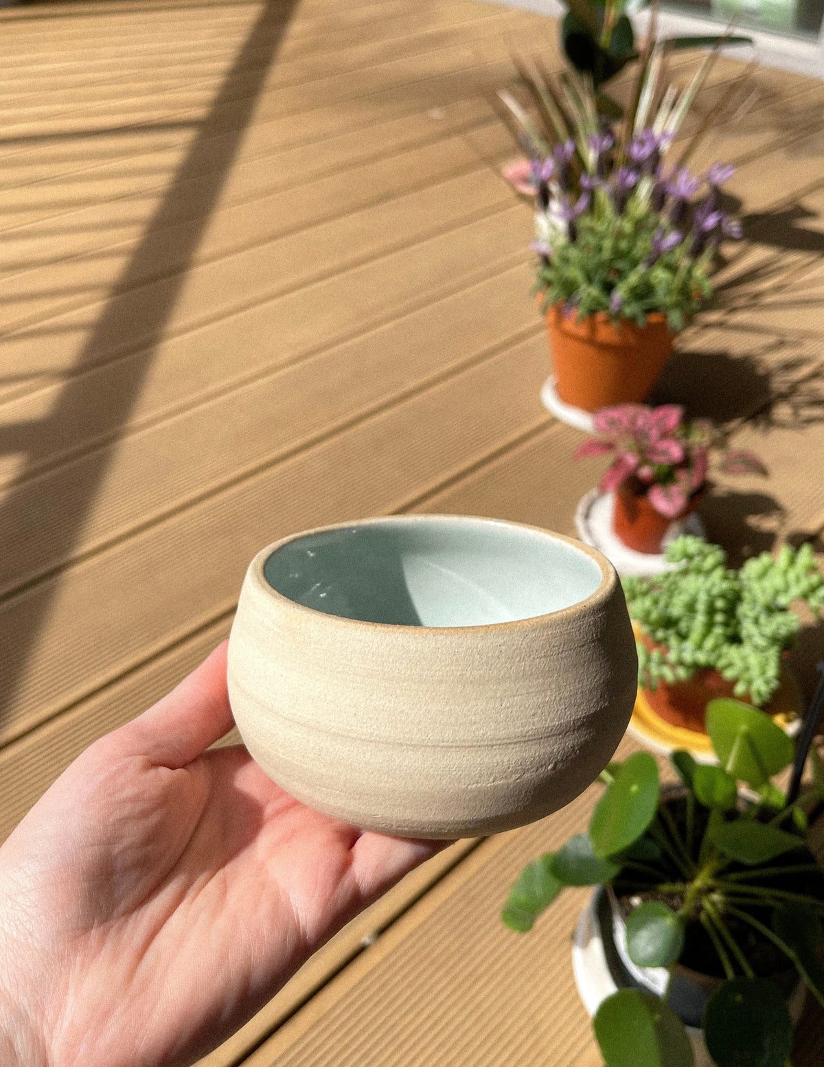 Hand holding small ceramic cup with blue-grey interior glaze outdoors